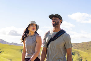 A man and a woman walking next to eachother with rolling hills behind them.
