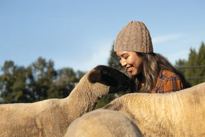 A woman next to some sheep wearing a beanie.