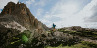 A picture of a man running up a trail to a mountain peak with blue skies in the background.
