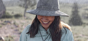 A woman wearing a Sunday Afternoons rain hat with rain pouring down.