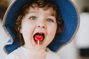 A picture of a kid eating a lolipop, wearing a Sunday Afternoons hat.