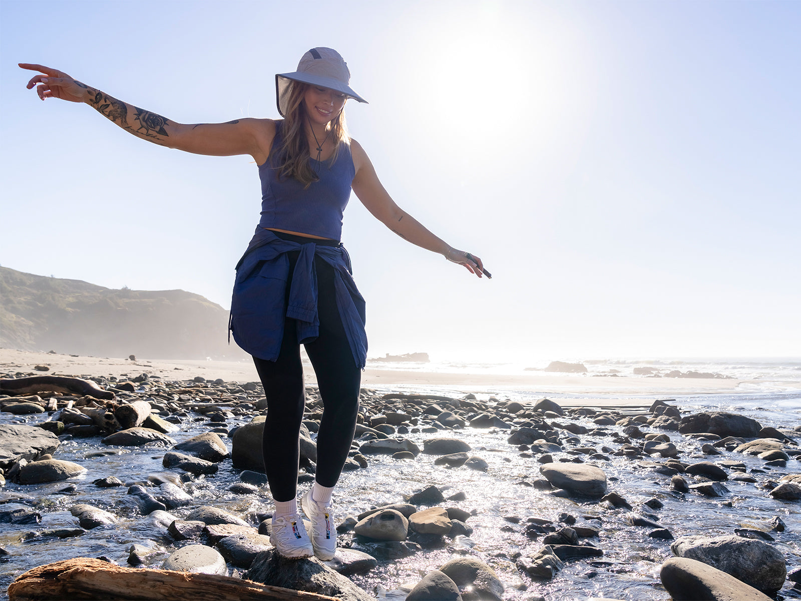 A woman walking on the beach wearing a Sunday Aftenroons Ultra Adventure Hat