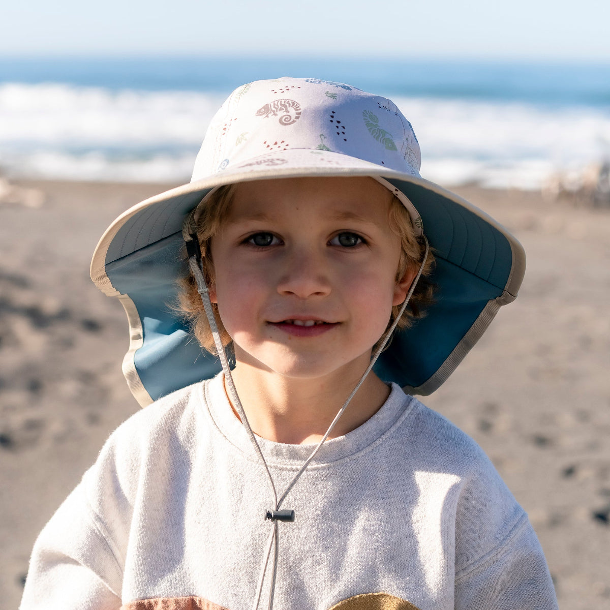 A boy wearing a Sunday Afternoons Kids' Play Hat in the Cream Chameleons color.
